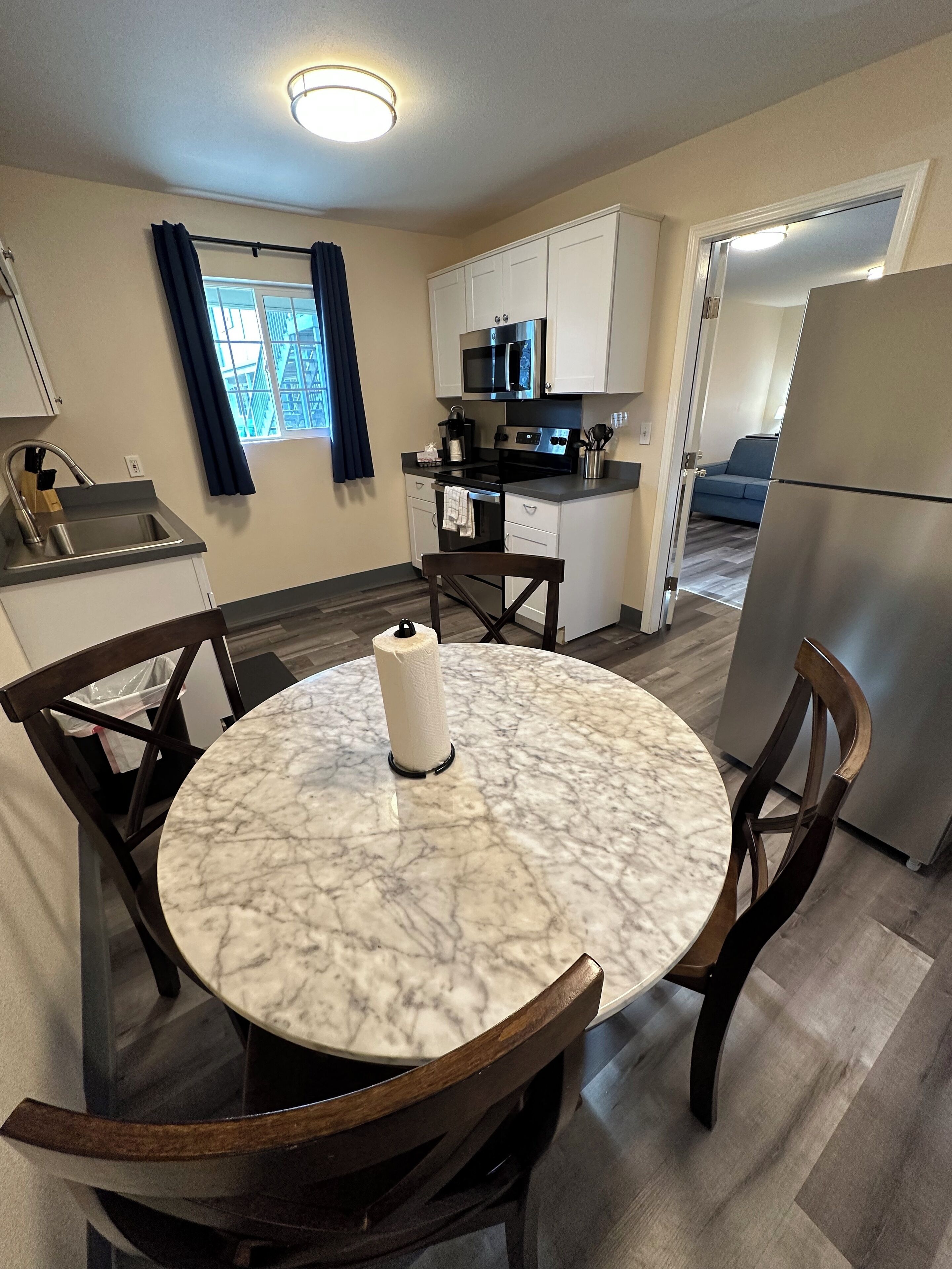 A compact kitchen with white cabinets, a black countertop, and a stainless steel refrigerator.