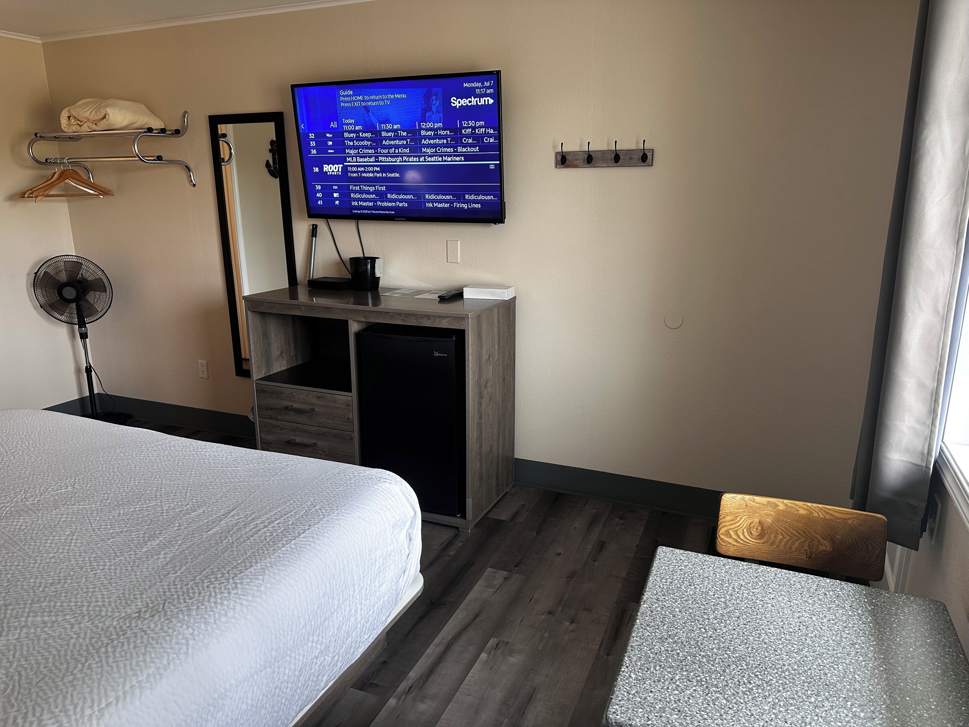 Quarto de hotel com cama, escrivaninha com computador, televisão na parede e um pequeno espaço de estar.