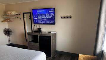 Quarto de hotel com cama, escrivaninha com computador, televisão na parede e um pequeno espaço de estar.