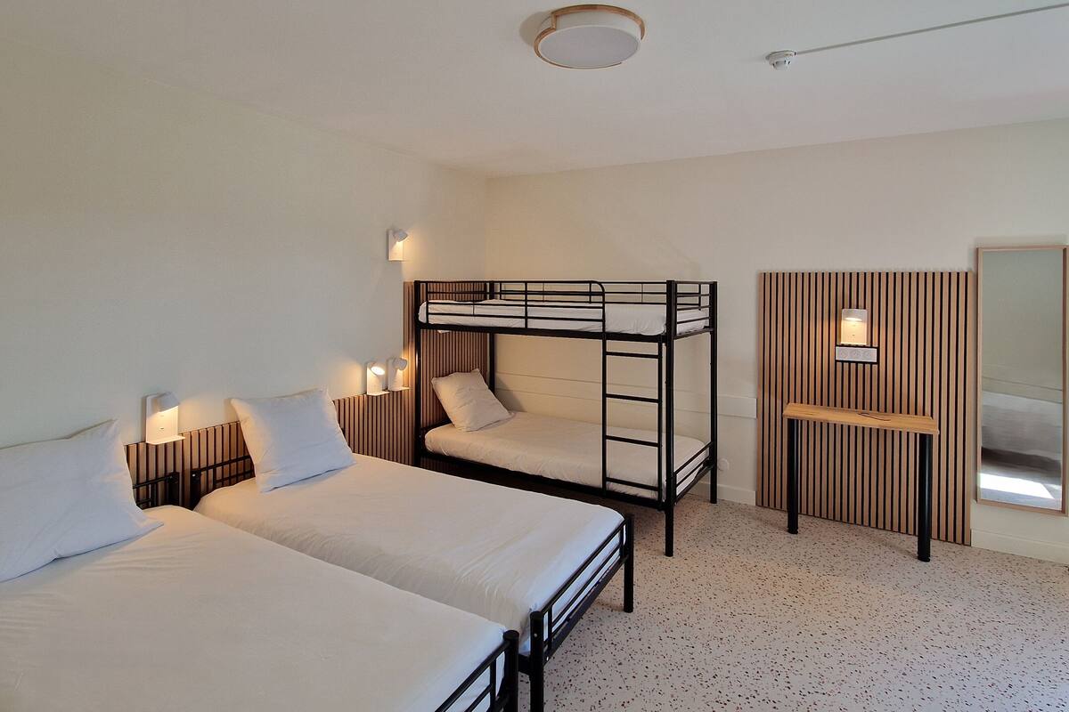 A room with two single beds, a bunk bed, a small wooden desk, and a mirror.