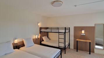 A room with two single beds, a bunk bed, a small wooden desk, and a mirror.