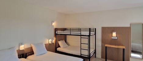 A room with two single beds, a bunk bed, a small wooden desk, and a mirror.