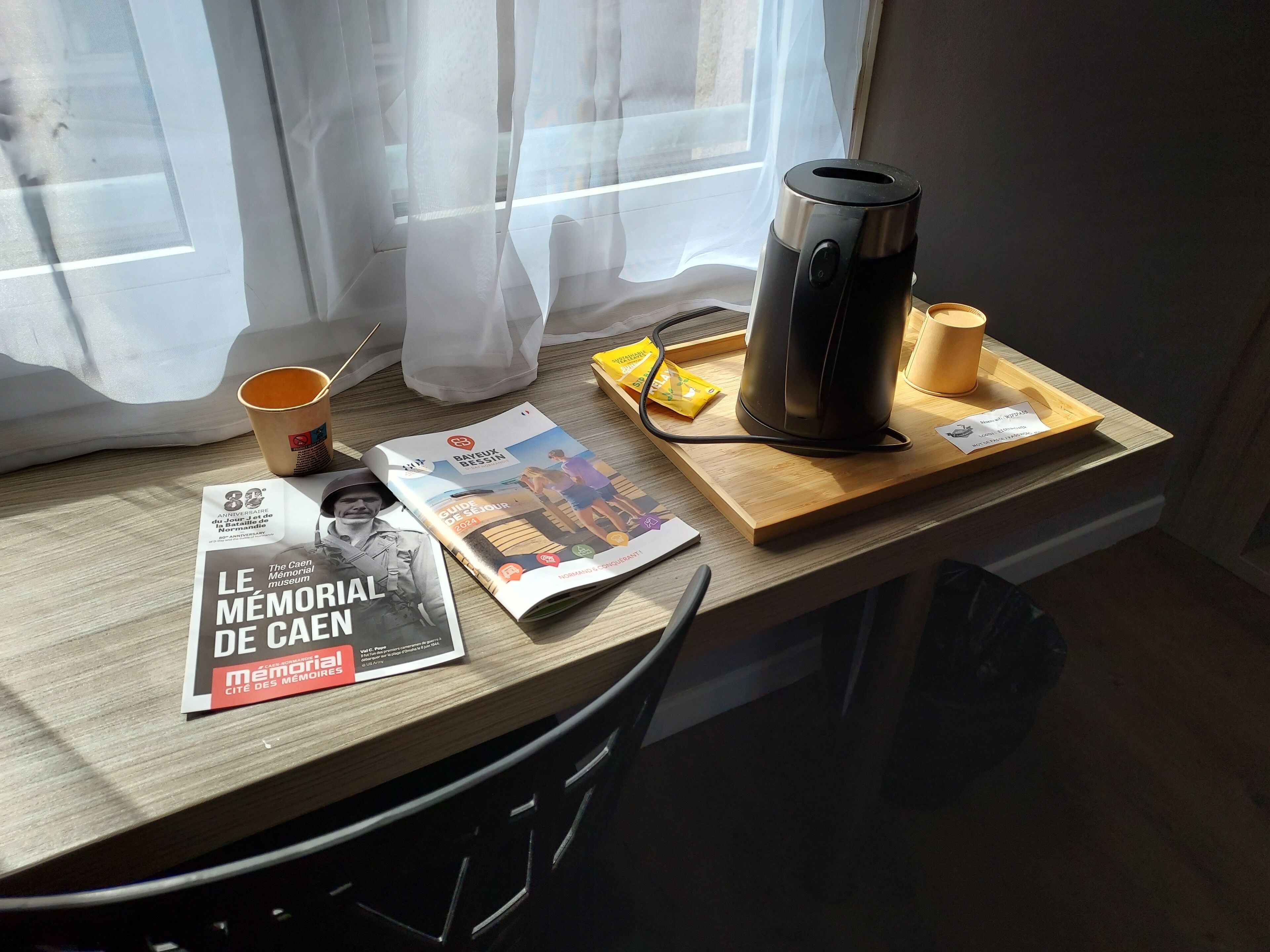 Une table avec une machine à café, une tasse, un magazine et un plateau sur lequel se trouvent un sac et un paquet.