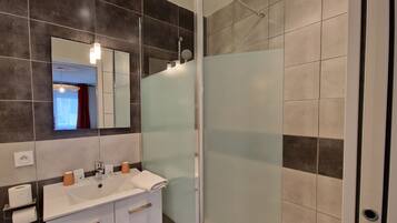 A modern bathroom with a glass shower enclosure, a white sink with a mirror above it, and dark tiled walls.