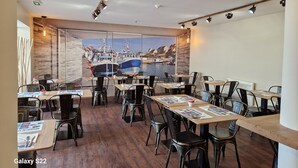 Un restaurante con mesas y sillas de madera, vista a barcos en el agua y un diseño moderno de techo.
