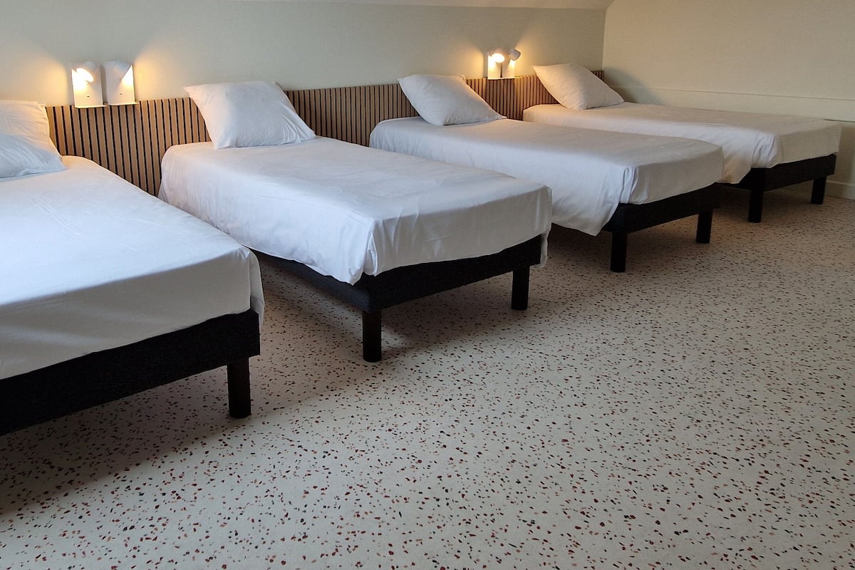 A hotel room with four single beds arranged in a row, each with a headboard and bedside lamps.