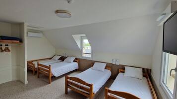Une chambre de dortoir avec trois lits en bois, un ventilateur de plafond, un appareil de climatisation et une fenêtre laissant entrer la lumière naturelle.