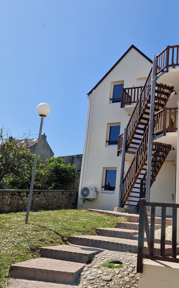 Un edificio de varios pisos con una escalera de madera, una antena parabólica y un muro de piedra al fondo.