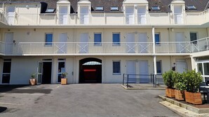 Un hotel de varios pisos con entrada central, balcones y un área de estacionamiento.