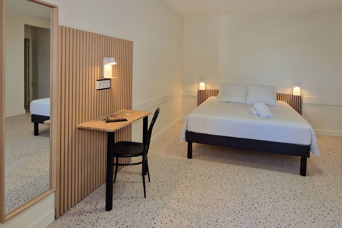 A hotel room with a bed, a desk, a chair, a mirror, and two bedside lamps.