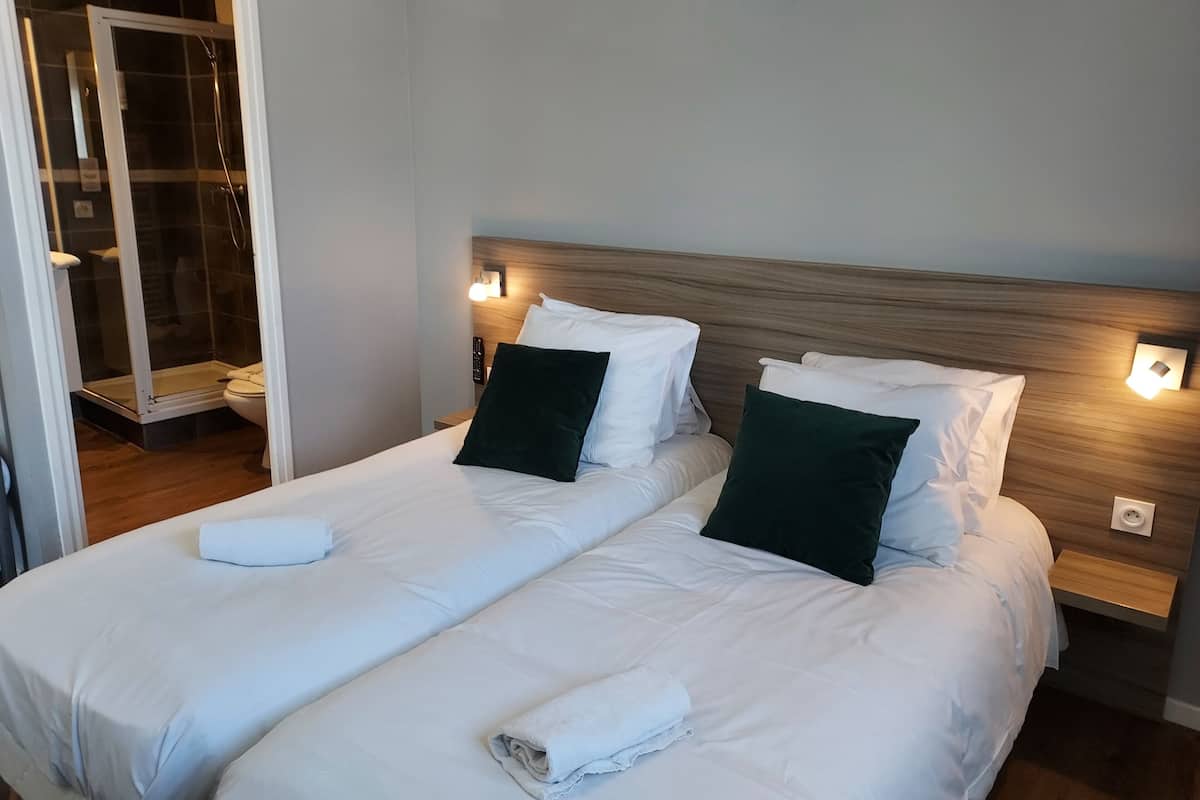 A hotel room with two beds, a wooden headboard, and a glass shower enclosure.