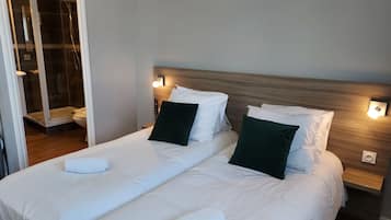 Quarto de hotel com duas camas, cabeceira de madeira e box de vidro.