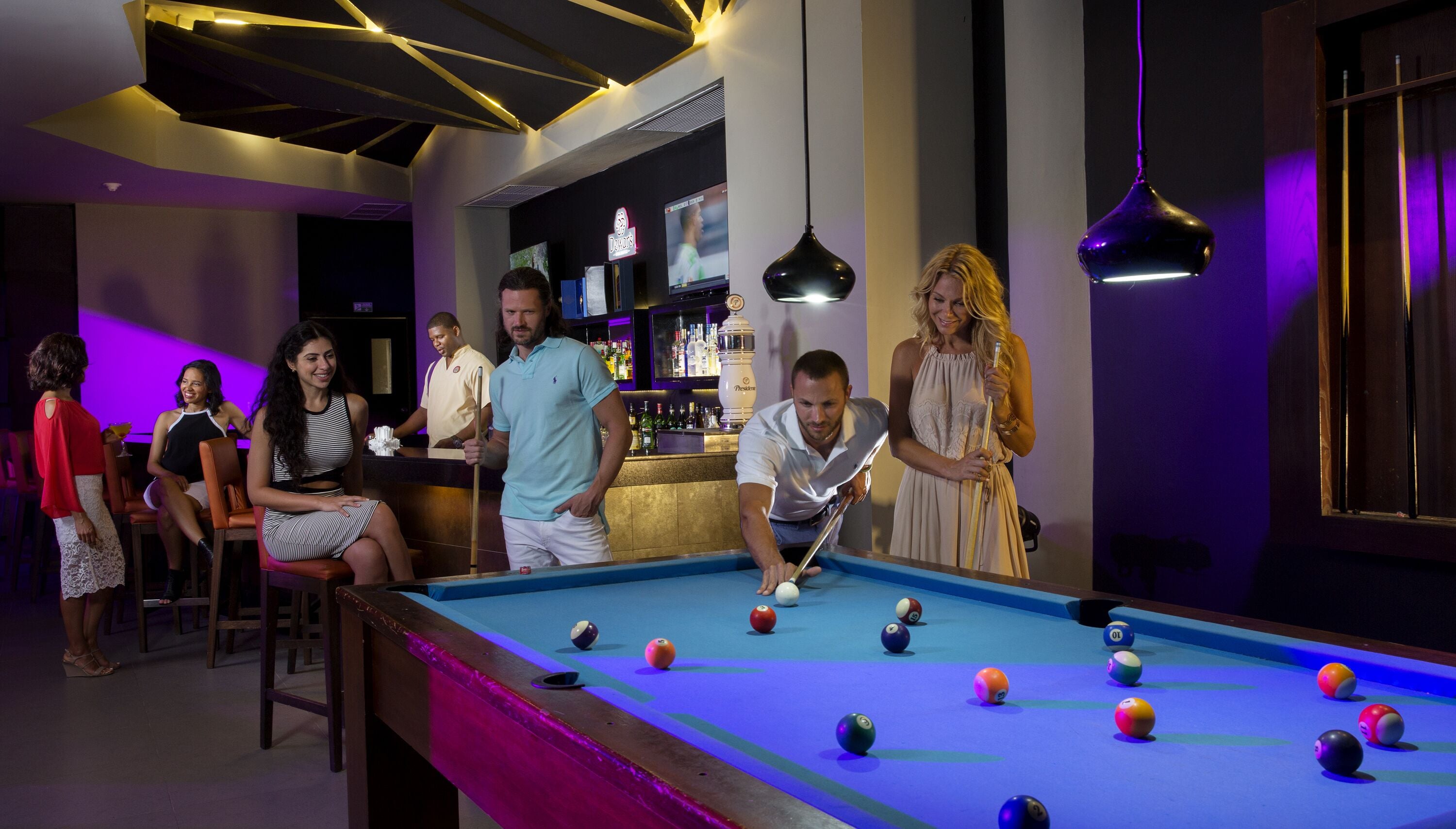 A pool table in a room with a bar area in the background.