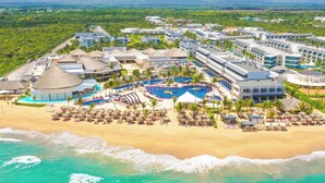 A resort with multiple buildings, a large central pool, and a beach area with sun loungers.