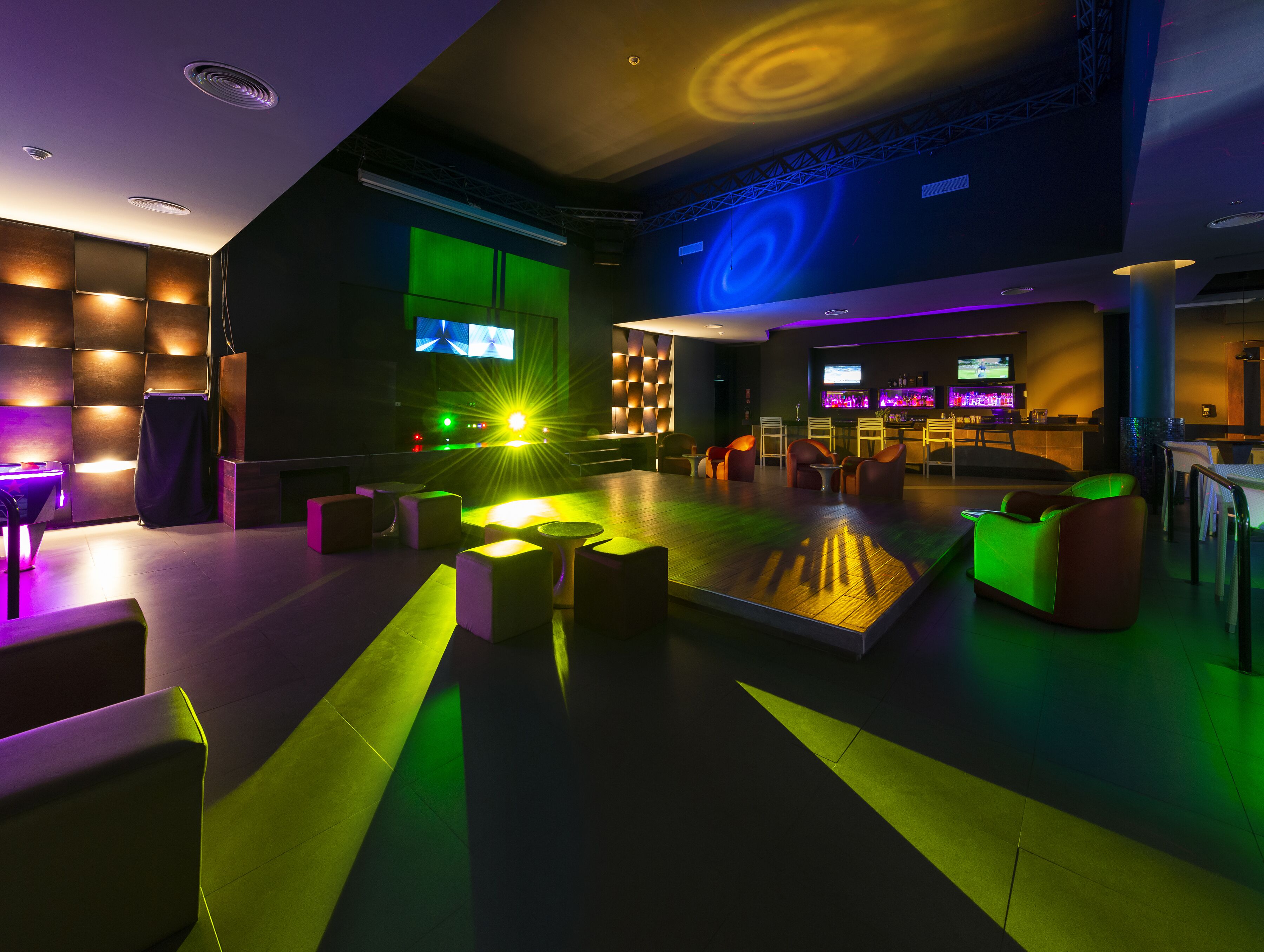 Un espacio lounge moderno con asientos, una barra y una pantalla grande mostrando un evento deportivo.