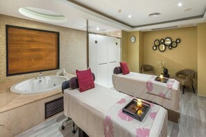 A spa room with two massage tables, a large bathtub, and a wall-mounted mirror.