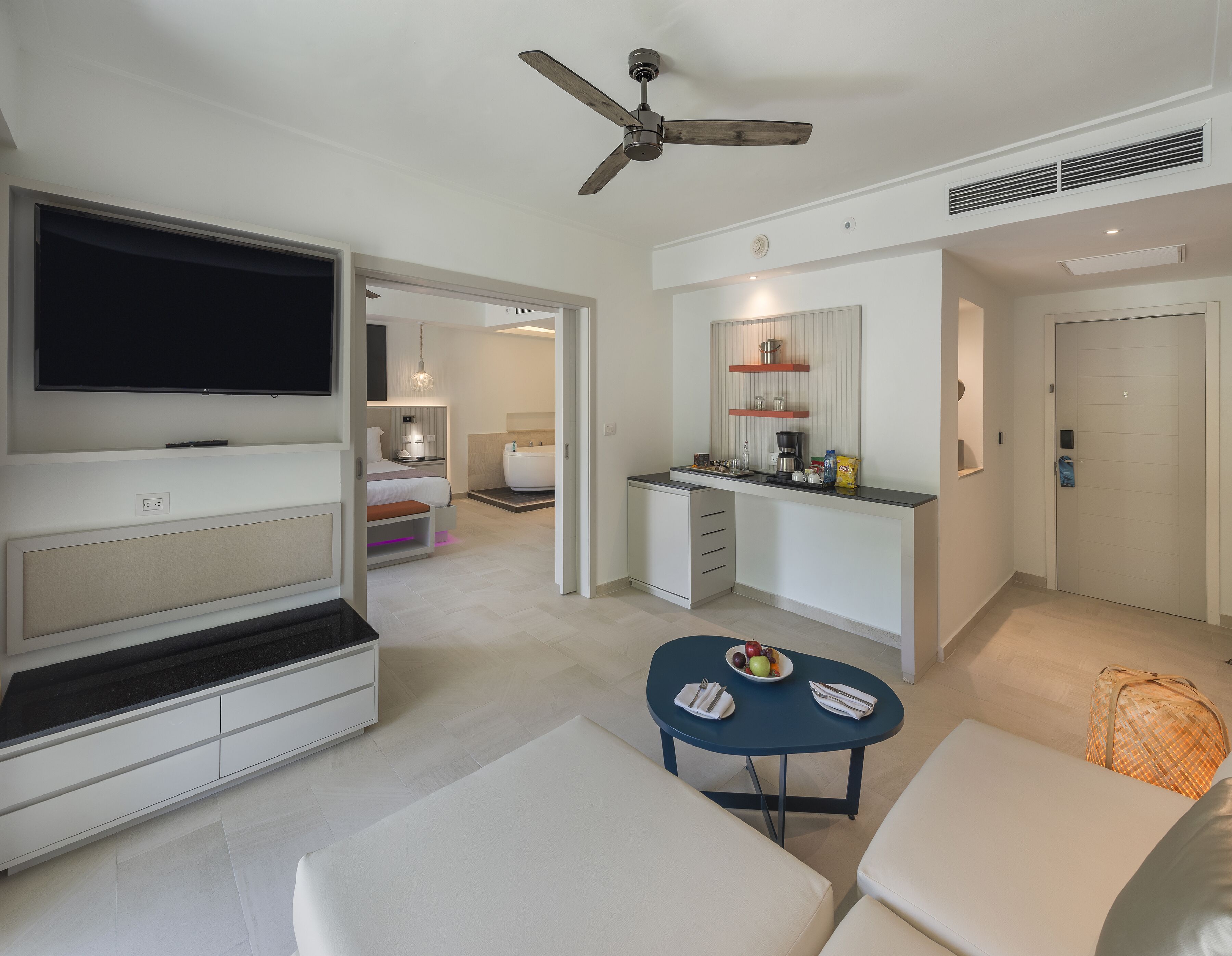 Una habitación de hotel moderna con televisión, zona de estar, kitchenette y baño.