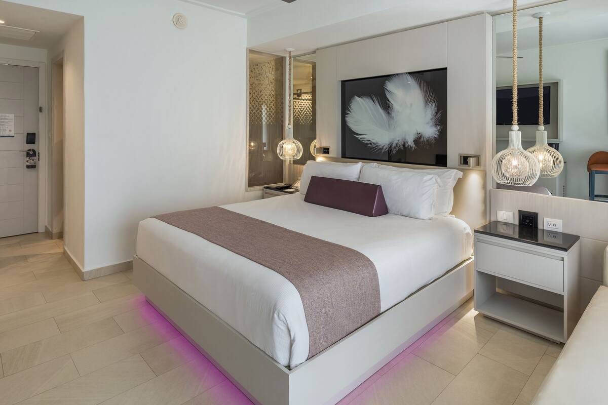 Moderni hotellihuone, jossa on suuri sänky, yöpöydät, peili ja yövalaisin.