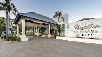 A hotel entrance with a covered patio, palm trees, and a sign reading "Royalty CHIC Punta Cana".