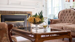 A living room with a fireplace, a floral arrangement on a glass table, and a tufted sofa. - Chestnut Inn Bed and Breakfast (Niagara Falls)