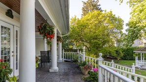 A covered porch with white columns, a white railing, and potted plants. - Chestnut Inn Bed and Breakfast (Niagara Falls)