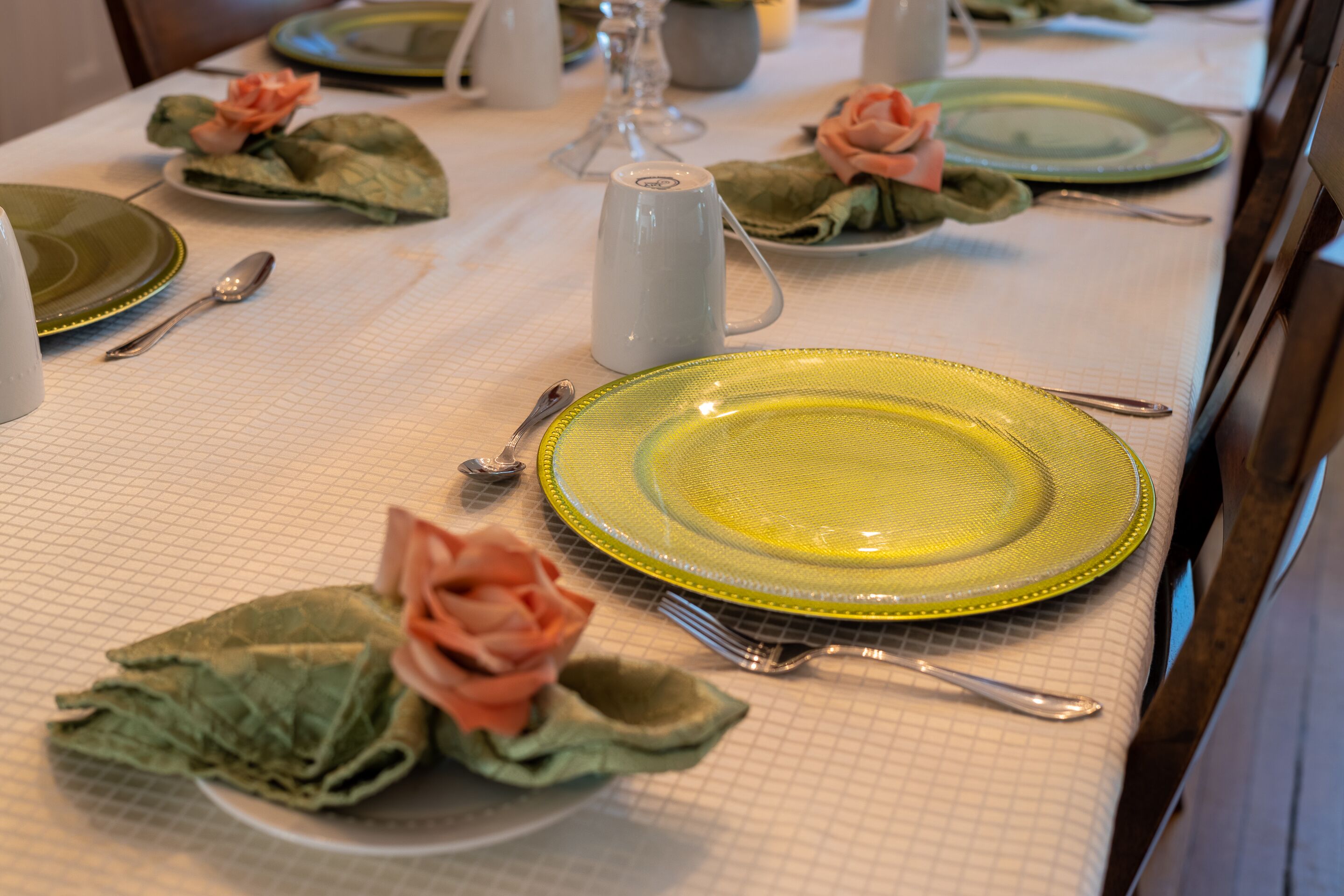 A table set with green plates, yellow plates, and green napkins folded into roses.