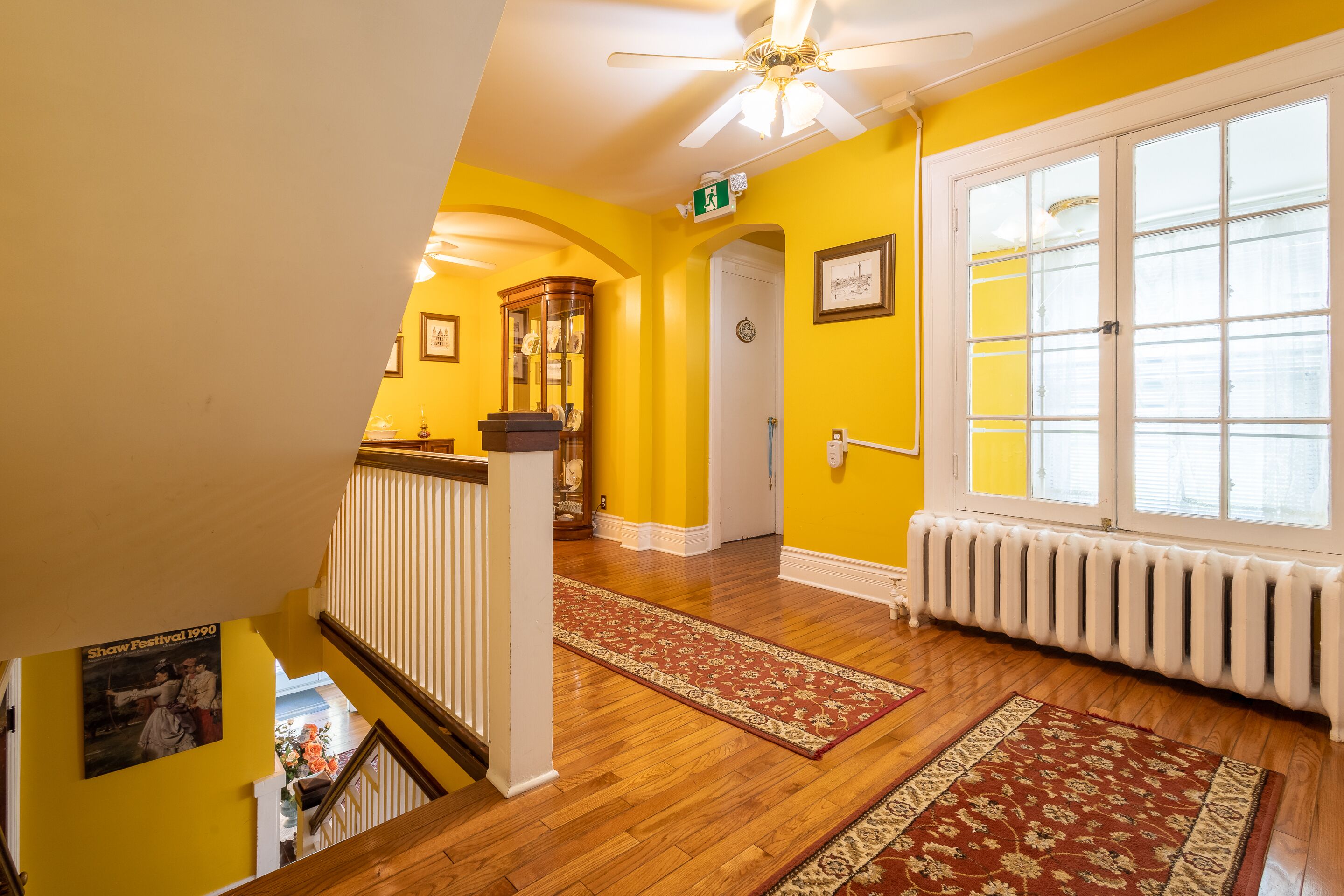 A staircase with wooden railings leading to a room with yellow walls, a radiator, and a large window.