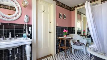 A bathroom with a white sink, a mirror, a white door, a chair, and a bathtub.