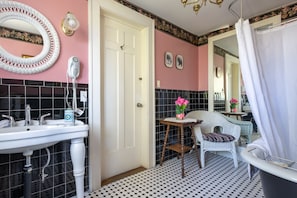Une salle de bain avec un lavabo blanc, un miroir, une porte blanche, une chaise et une baignoire.