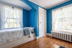 Une chambre avec un lit, un radiateur et une fenêtre ornée de rideaux légers.