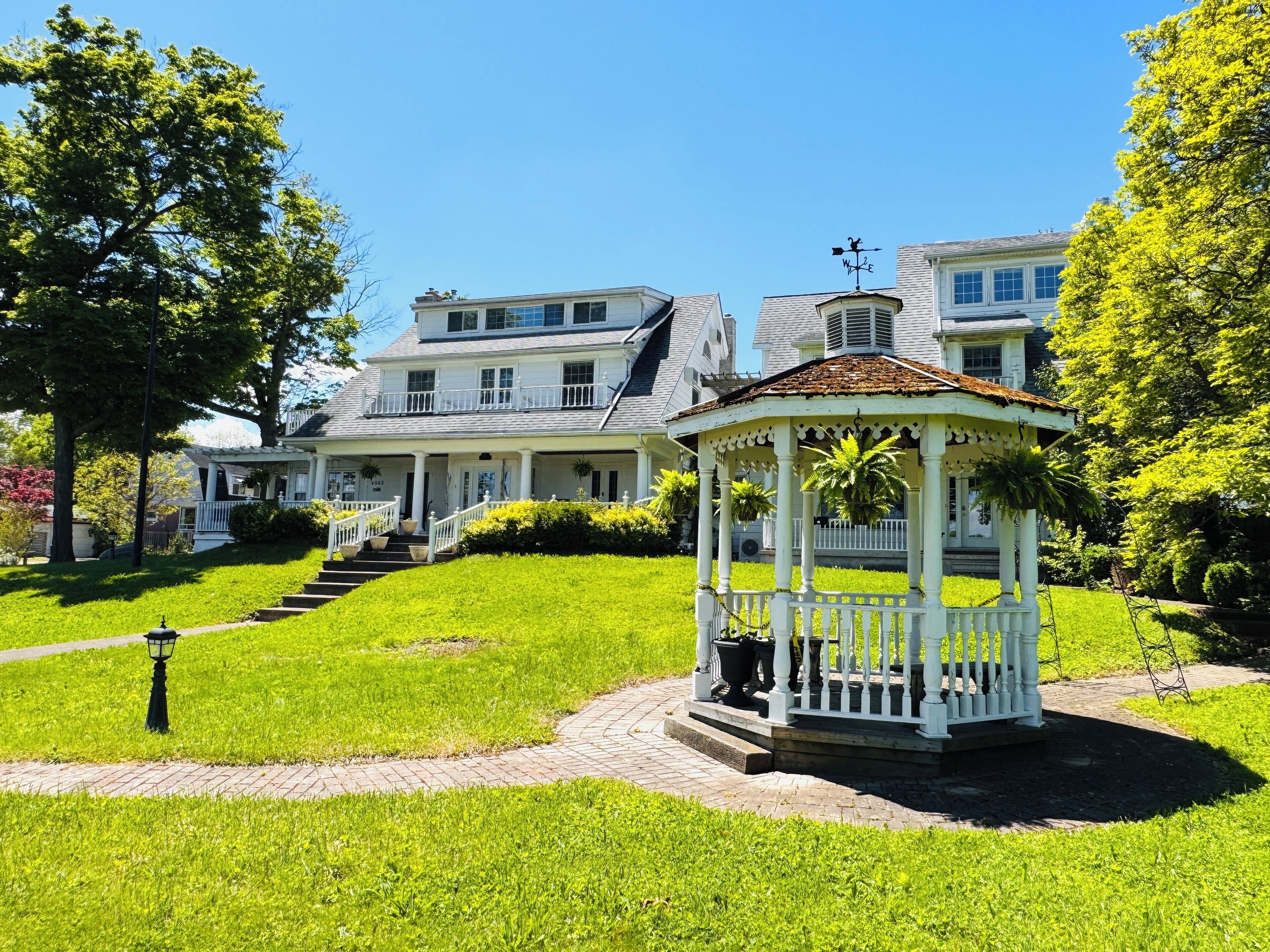 A gazebo with a white railing and a small roof, surrounded by well-maintained grass and a brick pathway.