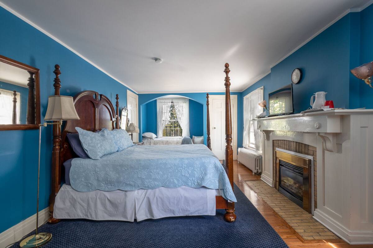 A bedroom with a four-poster bed, a fireplace, and a large window with a view of the outdoors.