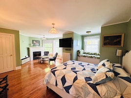 Un dormitorio con una cama grande, chimenea, televisor y un asiento junto a la ventana.