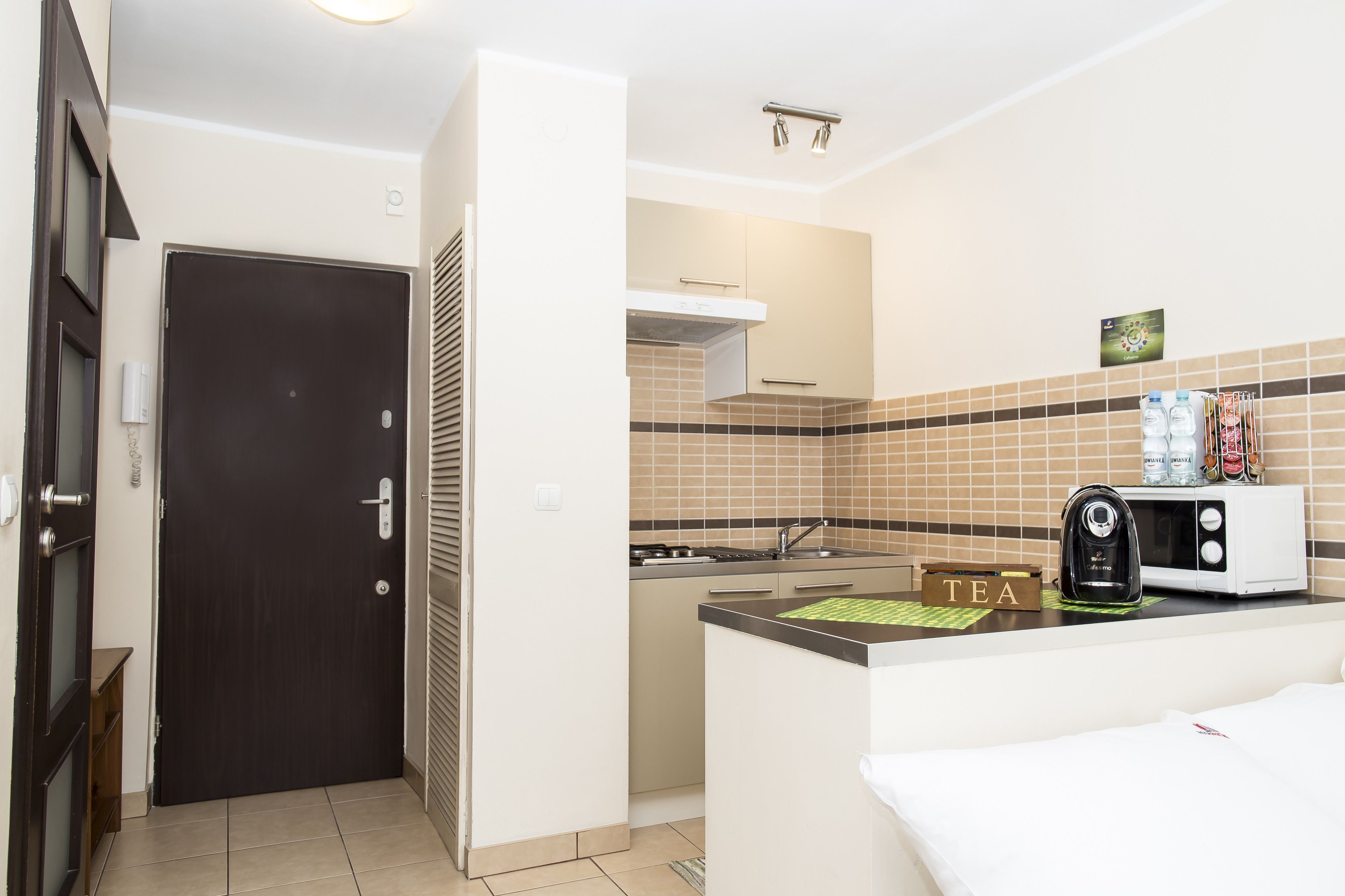 A compact kitchen with a microwave, tea box, and a small refrigerator.