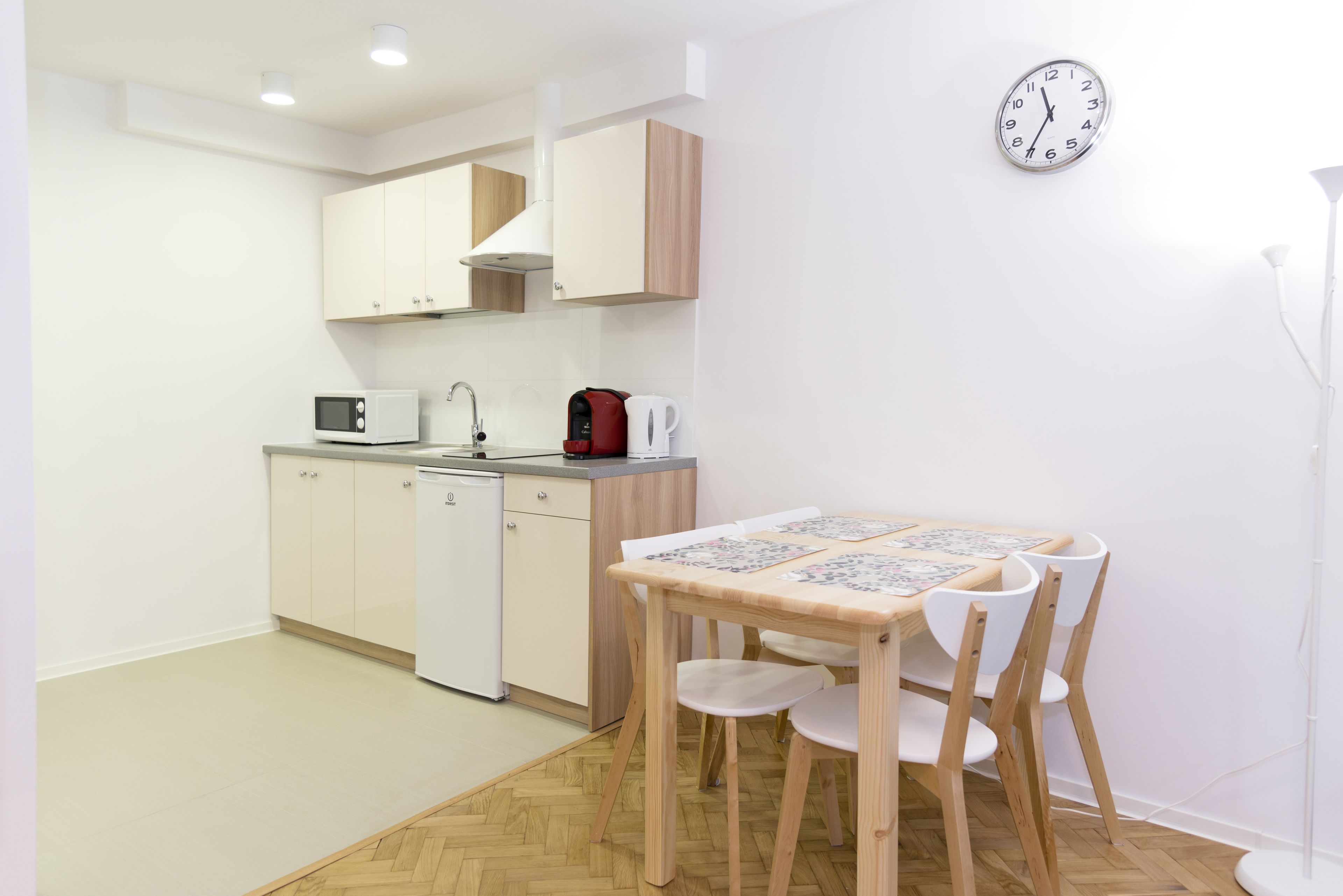 Una pequeña cocina con armarios blancos, un microondas, una tetera y una mesa de madera con sillas.