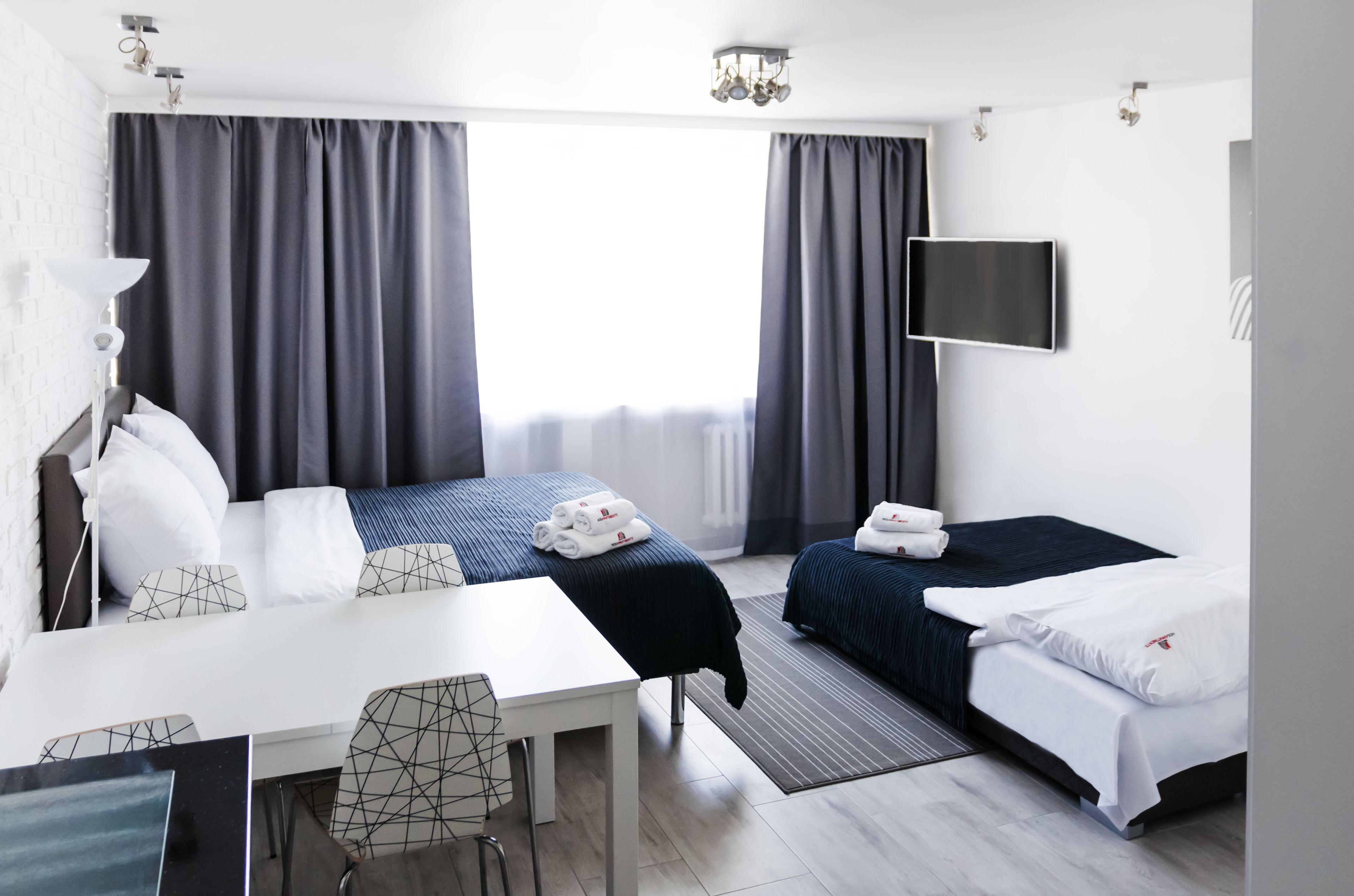 A modern hotel room with a bed, a desk, a chair, a TV, and a window with curtains.