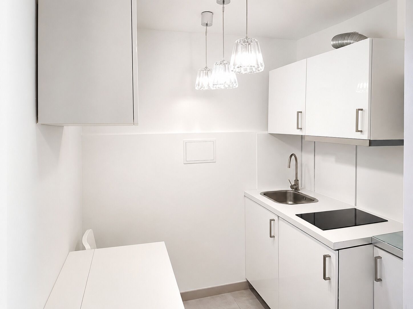 Una cocina moderna con armarios blancos, un lavamanos de acero inoxidable e iluminación colgante.