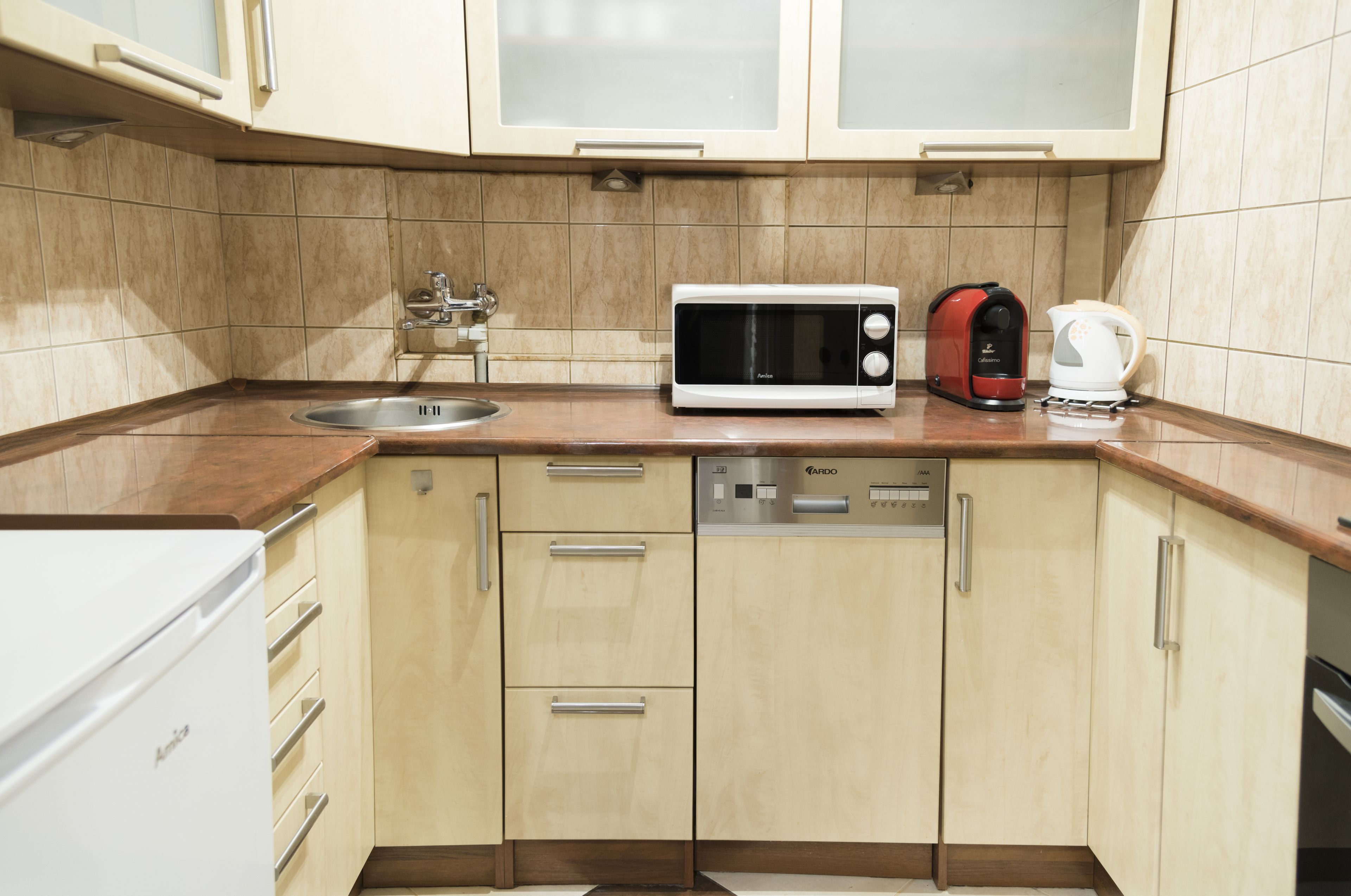 A kitchen with a microwave, kettle, sink, and dishwasher.