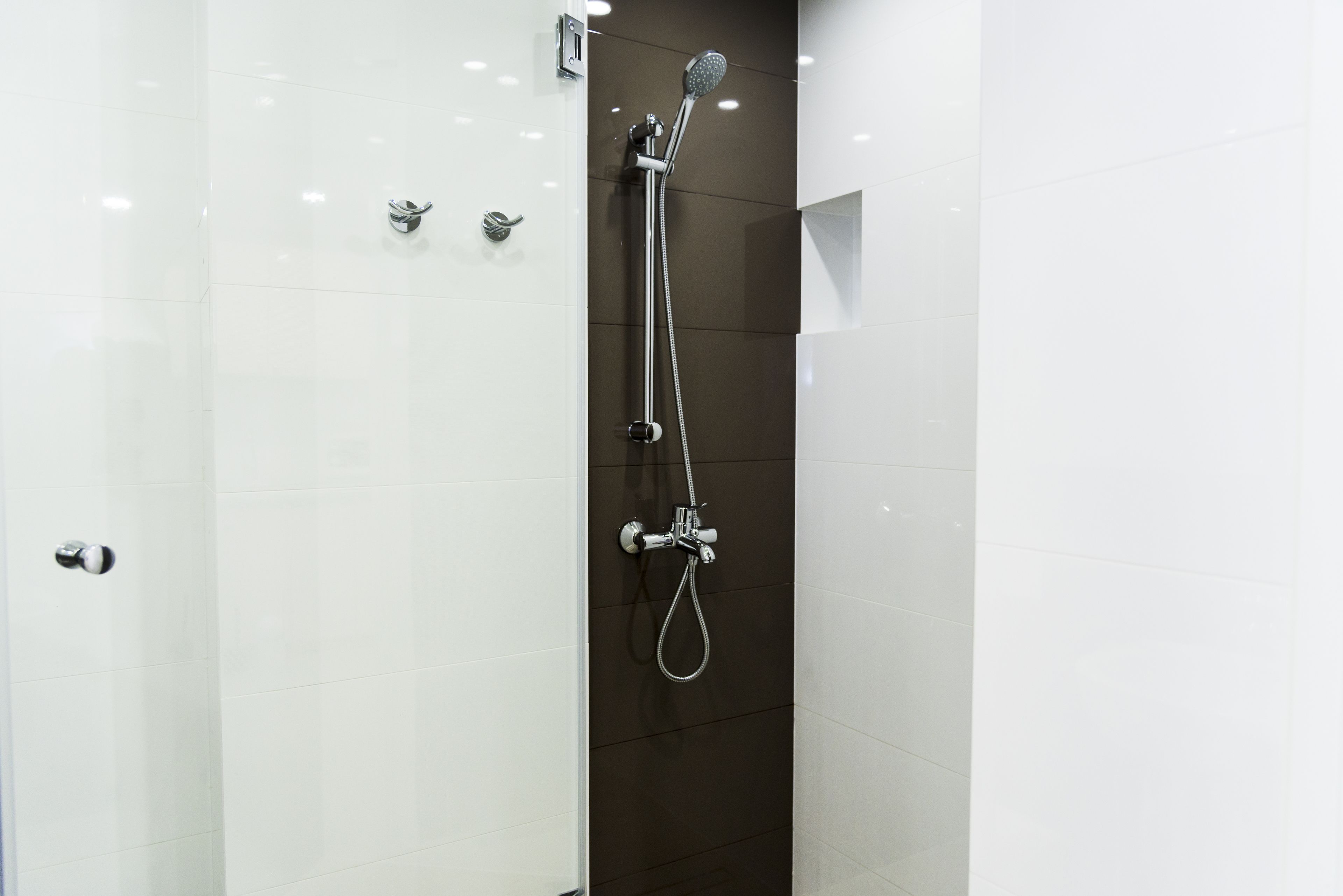 Ducha moderna con un cabezal de ducha de mano y un cabezal de ducha fijo, montada en una pared con un revestimiento de azulejos oscuros.