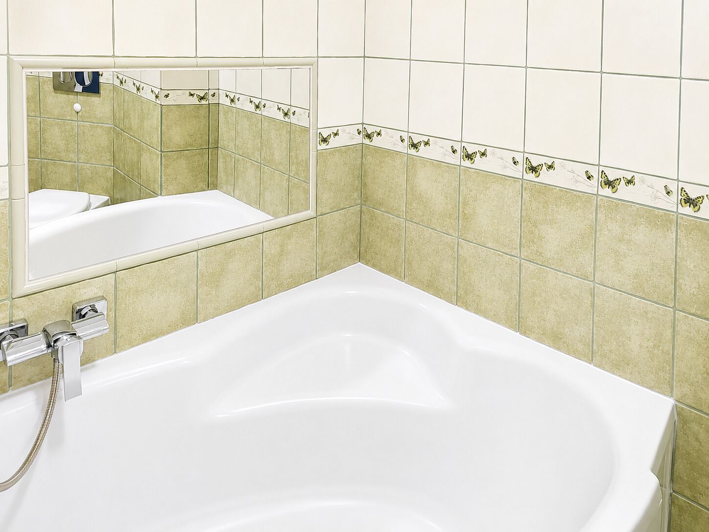 A bathroom with a bathtub, a mirror, and green-tiled walls.