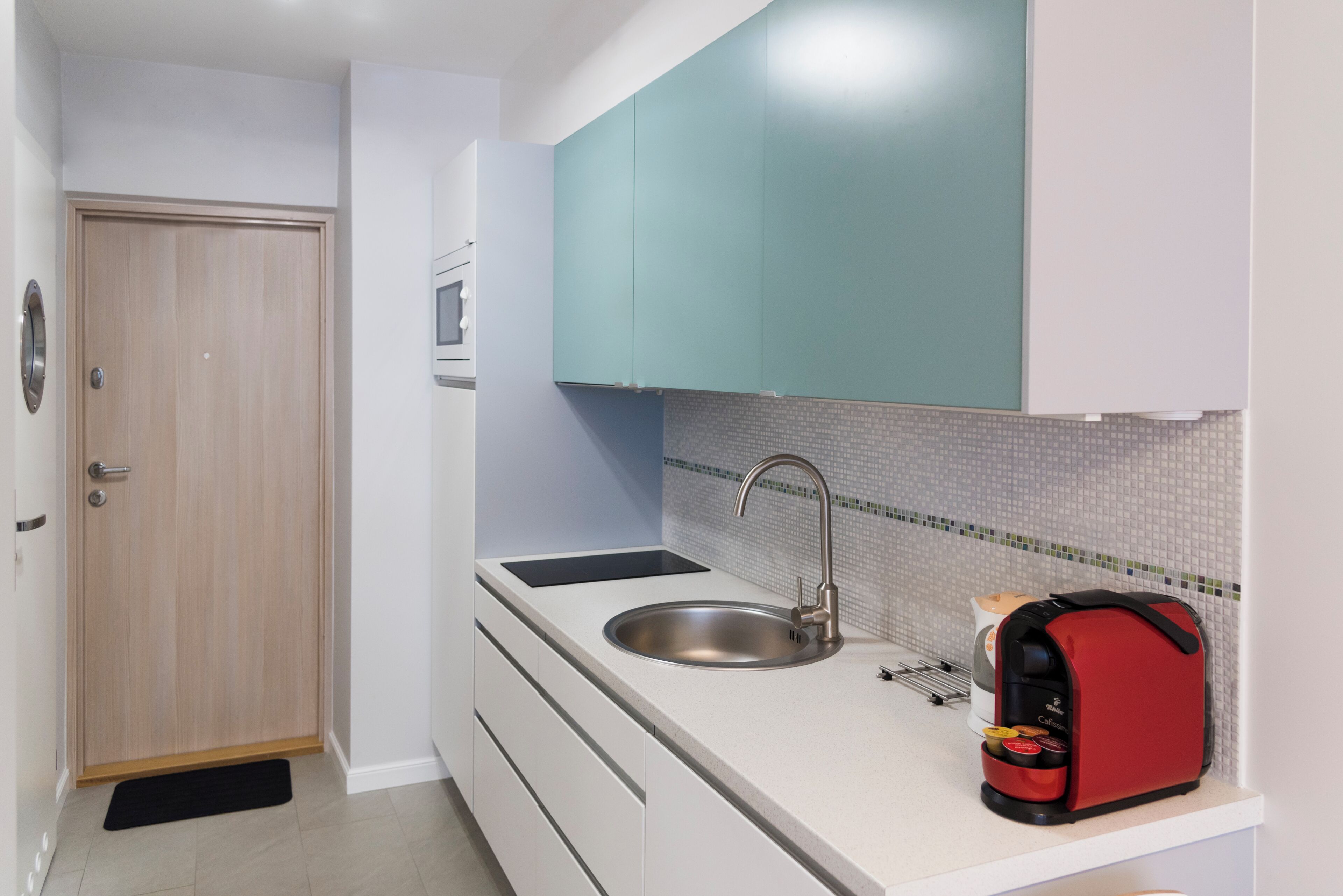 A compact kitchen with a sink, a red coffee maker, and teal cabinets.