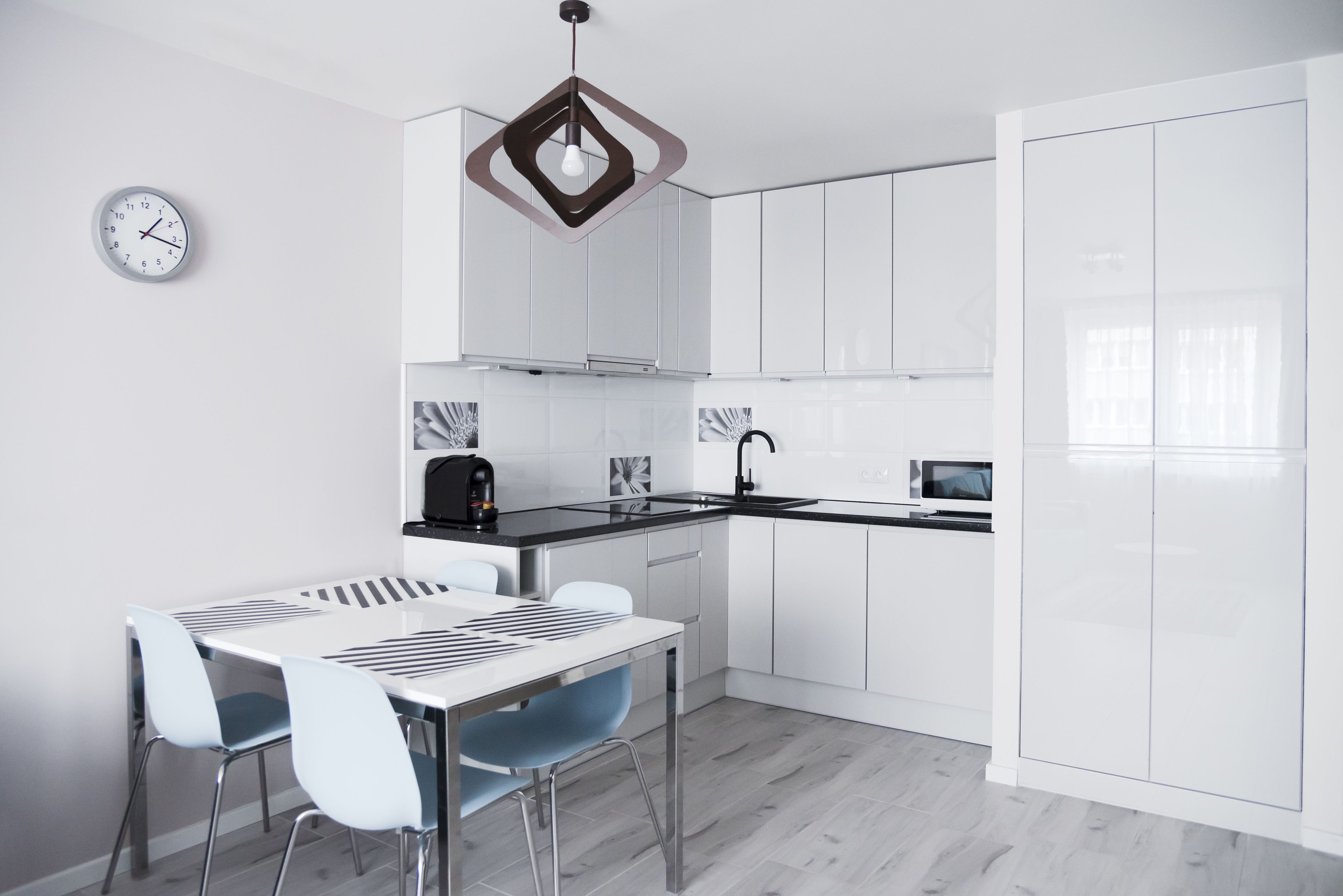 A modern kitchen with white cabinetry, a black countertop, a stainless steel sink, and a dining area with a white table and blue chairs.