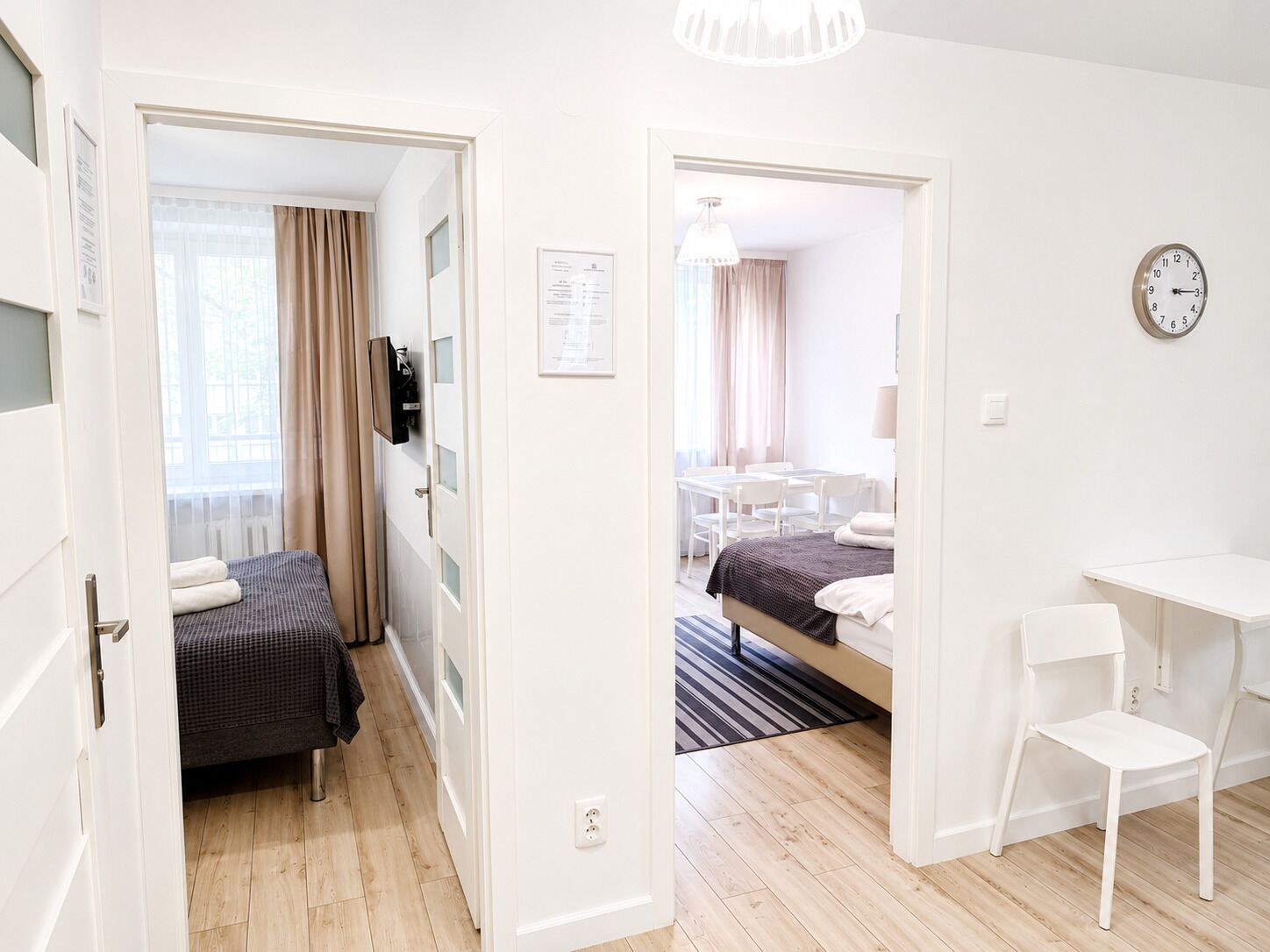 Ein Hotelzimmer mit einem Bett, einem Schreibtisch, einem Stuhl, einer Uhr und einer Tür, die in einen anderen Raum führt.