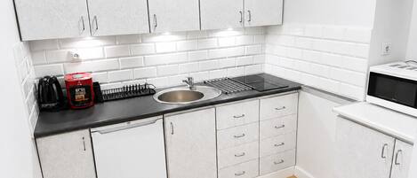 Una cocina con armarios blancos, encimera negra, pileta y microondas.