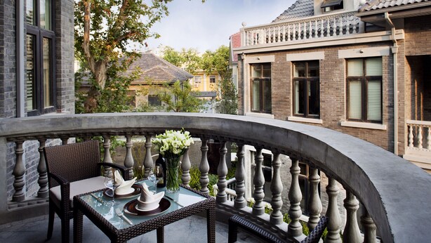 A balcony with wicker furniture, a glass table, and a vase of flowers. - Relais & Chateaux Yihe Mansions (Nanjing)