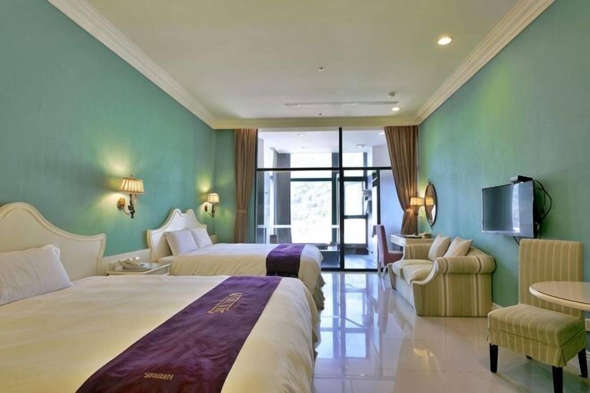 Habitación de hotel con dos camas, televisión, una silla y una mesita.