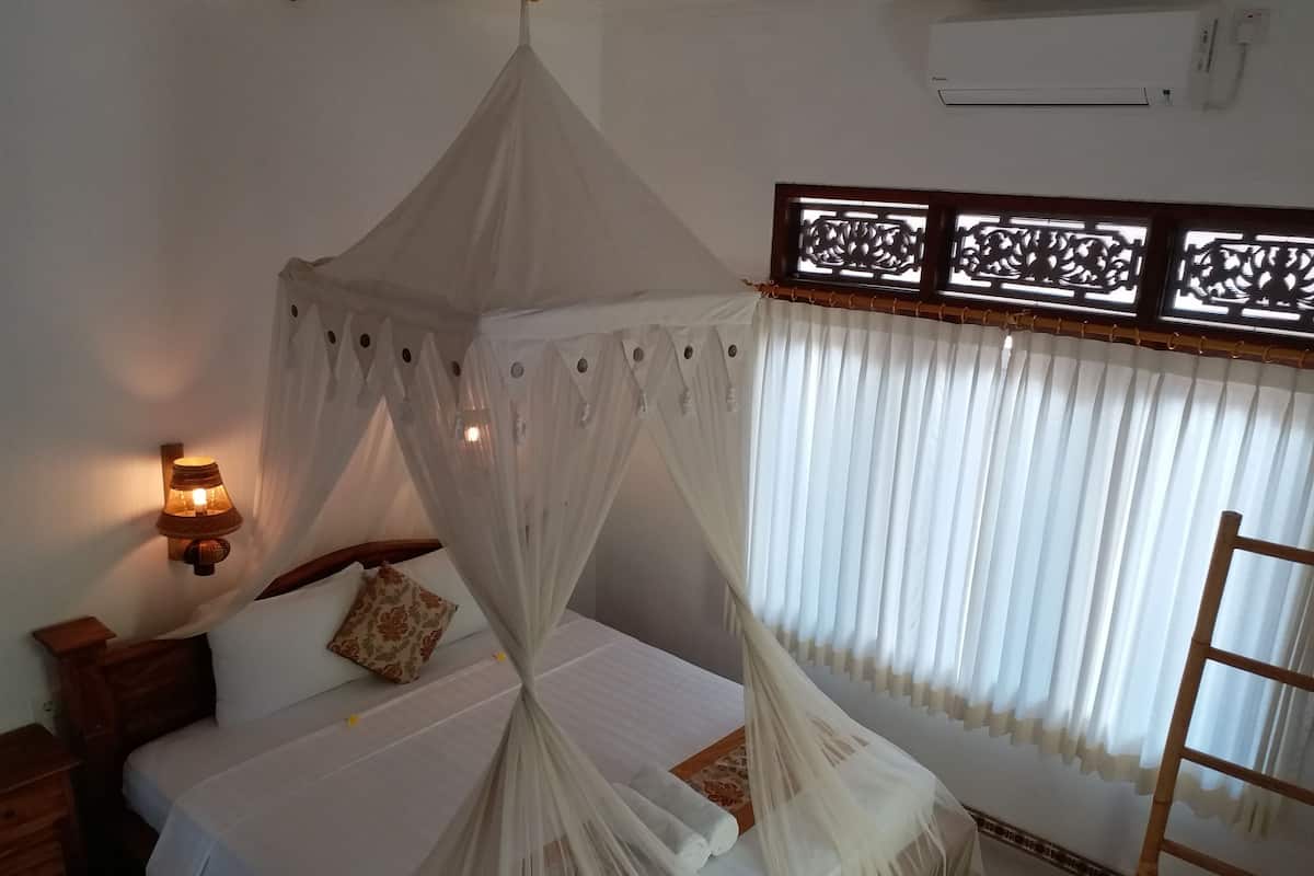 A bedroom with a canopy bed, a bedside lamp, a wooden nightstand, a window with curtains, and a wooden ladder.