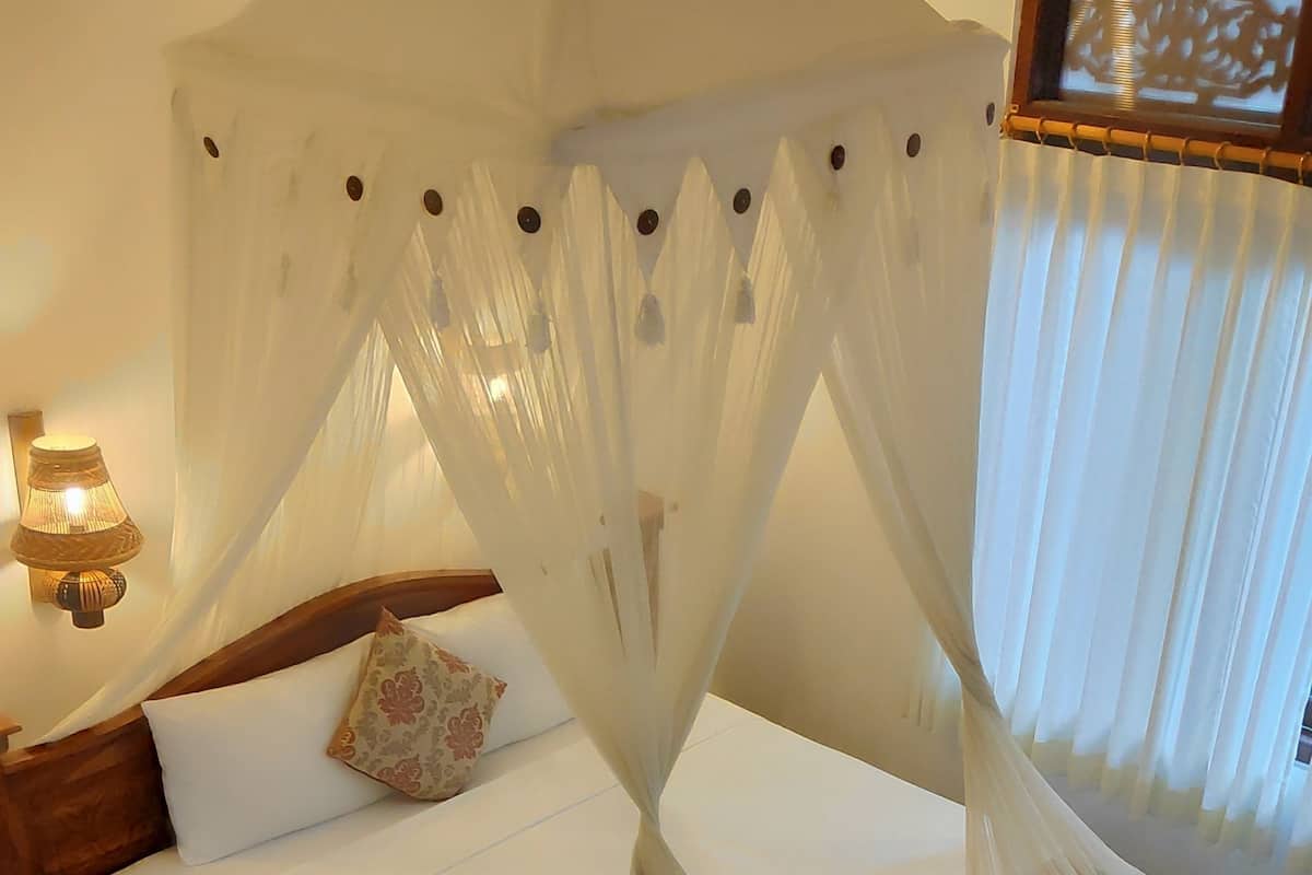 A bed with a canopy, a bedside lamp, and a framed picture on the wall.
