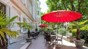 An outdoor patio with red umbrellas, potted plants, and outdoor seating. - Grand Hotel Bellevue - adults only (Merano)