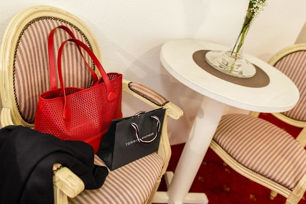 A chair with a striped cushion, a red handbag, a black shopping bag, and a small table with a vase of flowers.